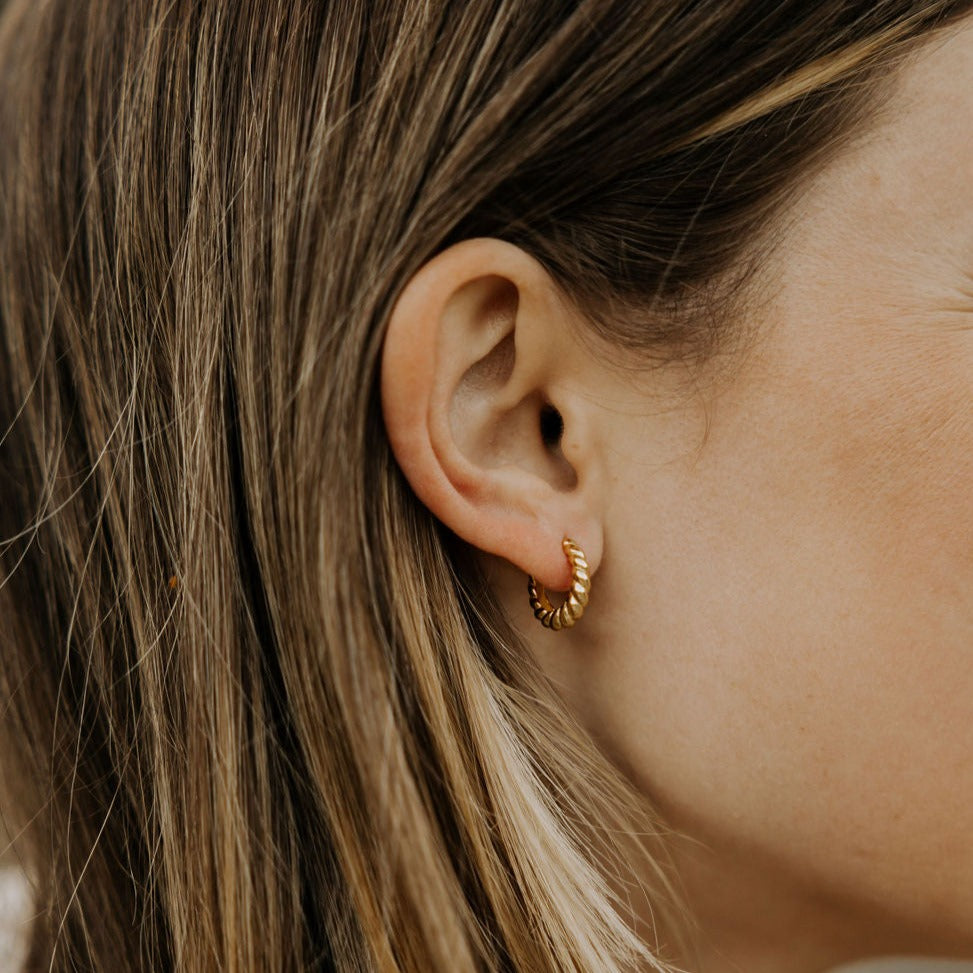 Close-up of a gold twisted hoop earring worn on an ear