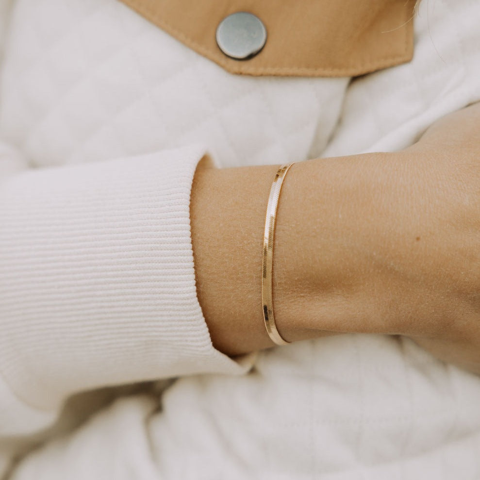 Close-up of a slim gold-filled herringbone bracelet on the wrist.