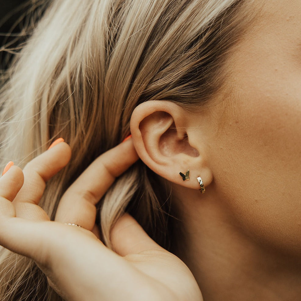 Gold butterfly mini stud worn beside a small hoop earring