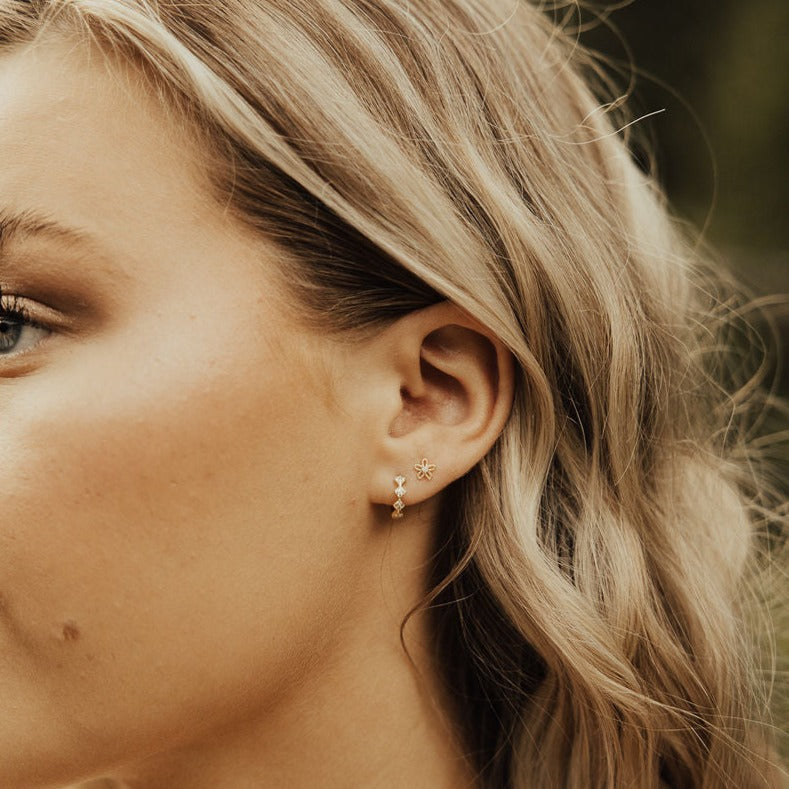 Gold diamond hoop earring worn with a small flower stud above it.