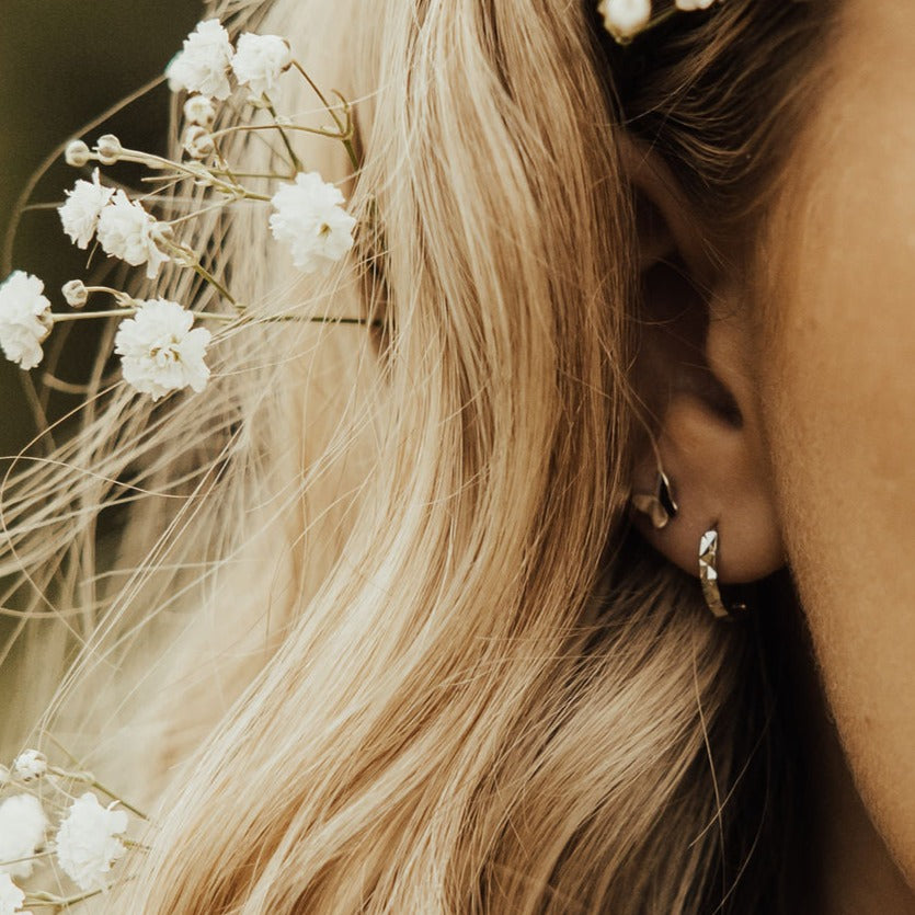Silver hammered hoop earring worn on an ear.