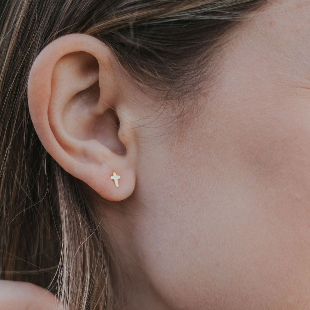 Light-colored cross stud earring with a gold-tone edge