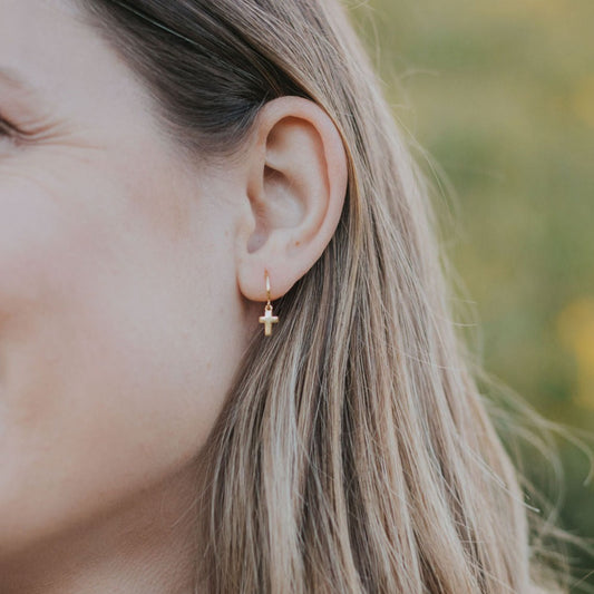 Gold-tone cross hoop earring worn on an ear