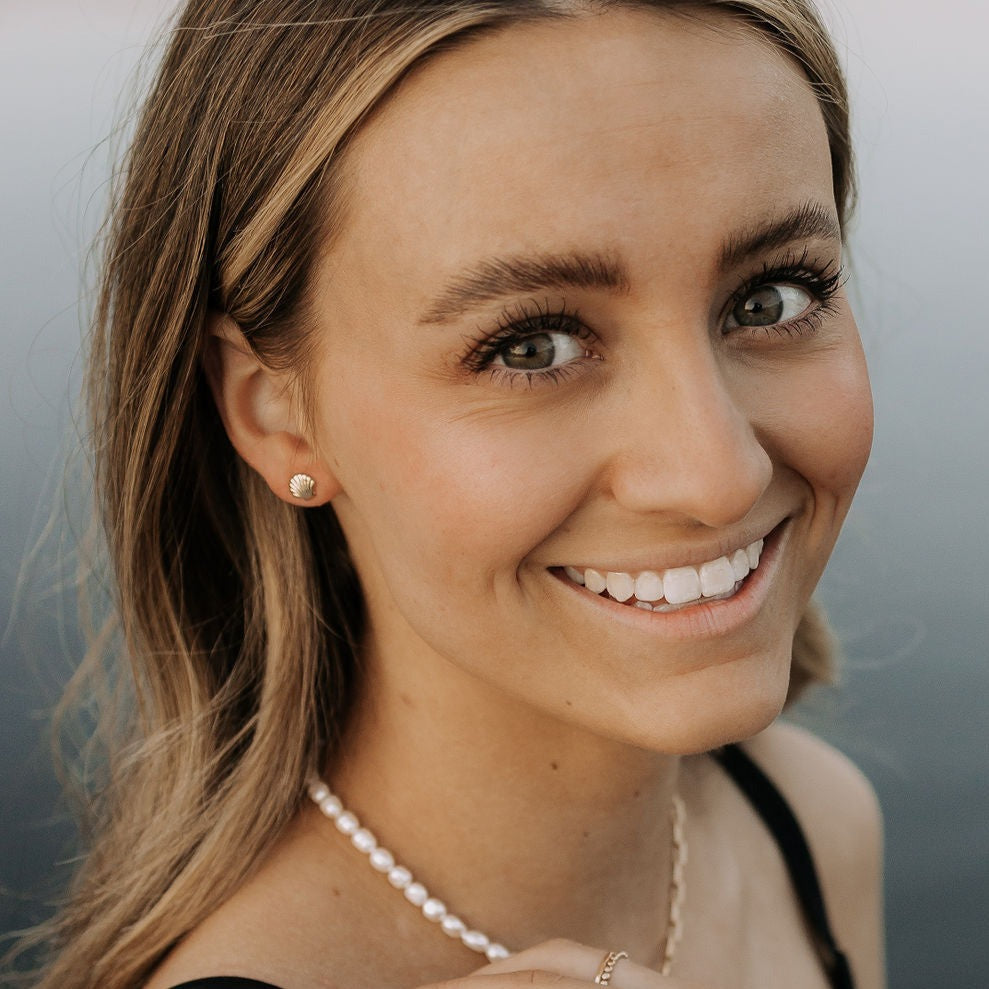 Small gold-tone sea shell stud earring worn on the earlobe