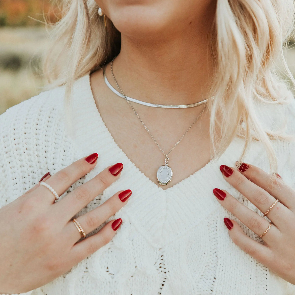 Silver oval locket necklace with a white pearlescent face, worn layered with a silver chain