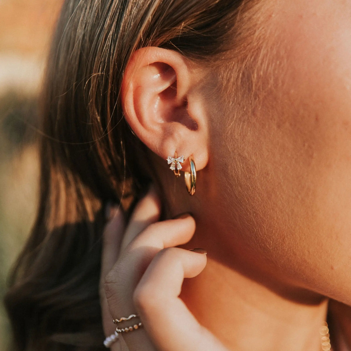 Gold diamond bow hoop earring worn beside a plain gold hoop