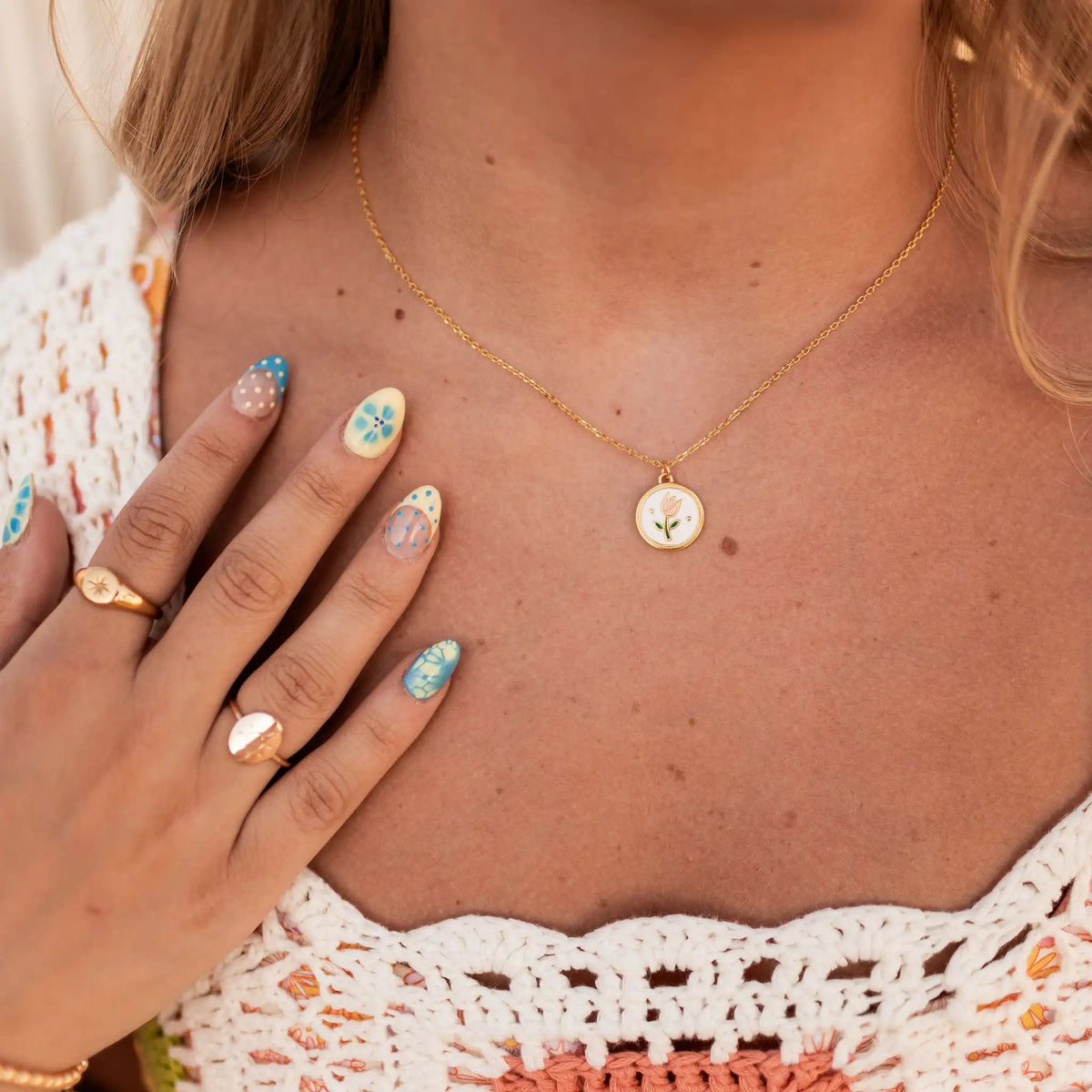 Gold necklace with a small round floral enamel pendant, worn at the neckline