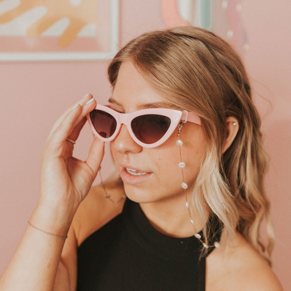 Pearl sunglasses chain with spaced beads hanging from pink sunglasses as they are adjusted.
