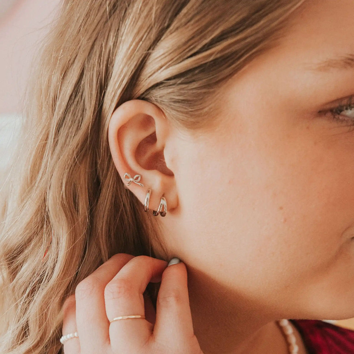 Gold bow stud worn with small dangling hoop earrings