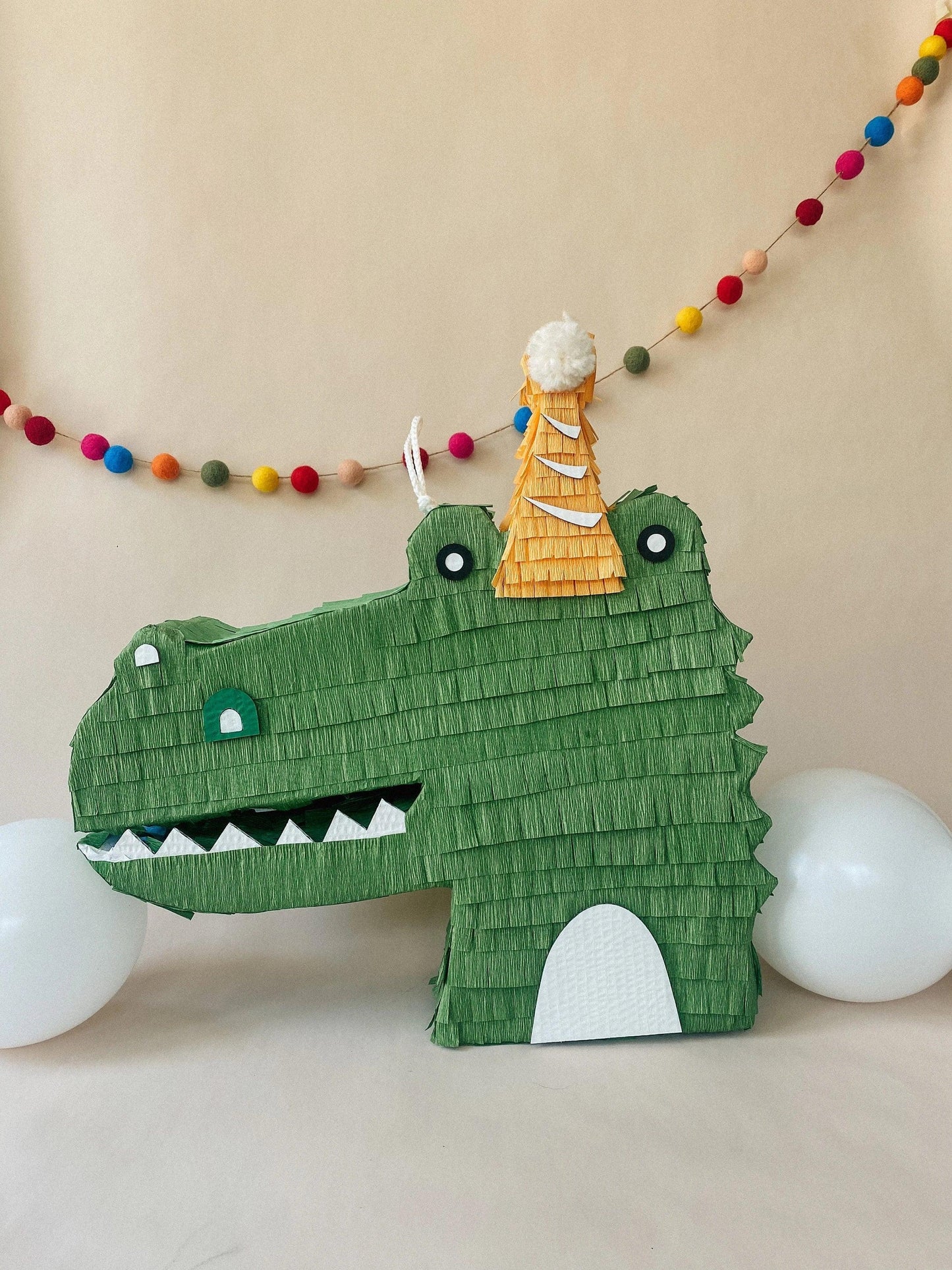 Green alligator piñata with open mouth, white tooth details, and central cream tree.