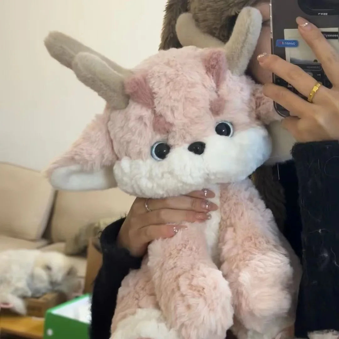 Pink plush dragon with antlers, held up, white muzzle and round black eyes