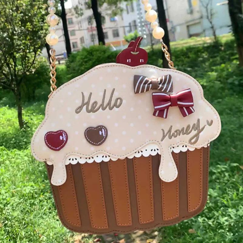 Cupcake-shaped shoulder bag with cream top, red bow, and striped brown base
