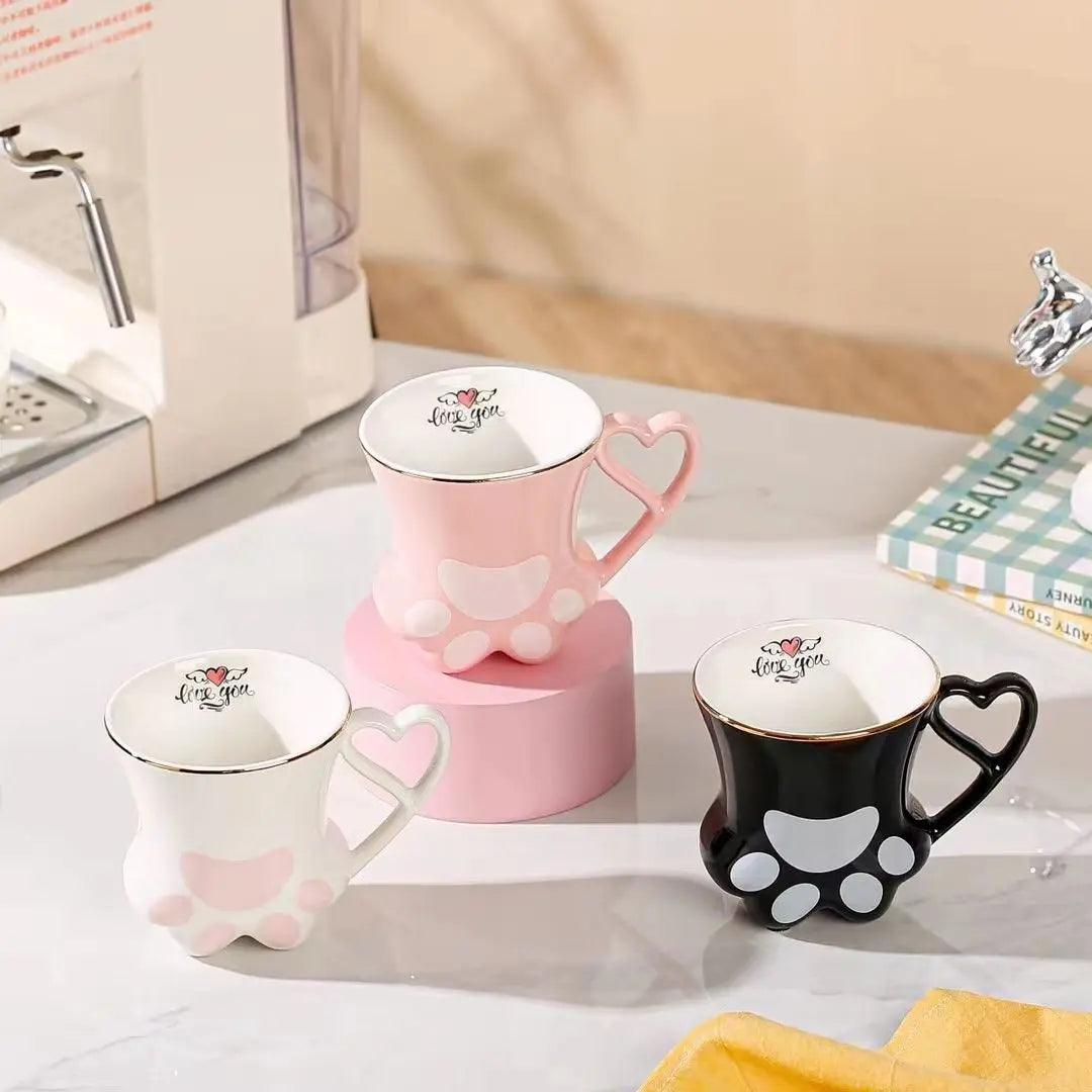 Three cat paw mugs in pink, white, and black with heart handles and paw pad designs