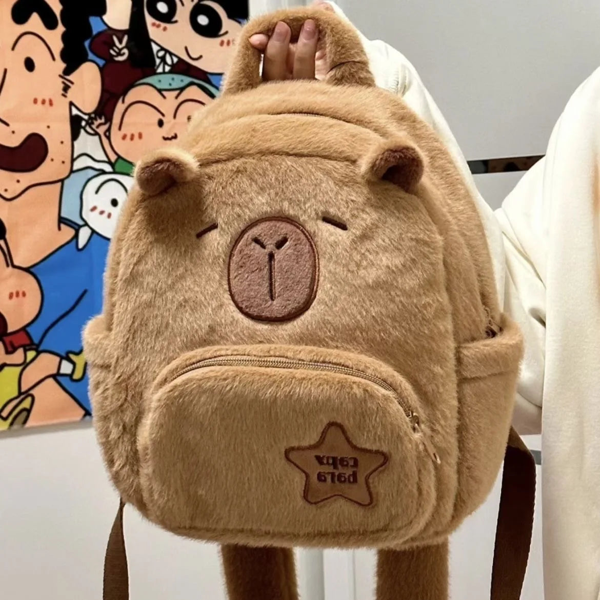 Tan capybara plush backpack with front zip pocket and raised star logo patch