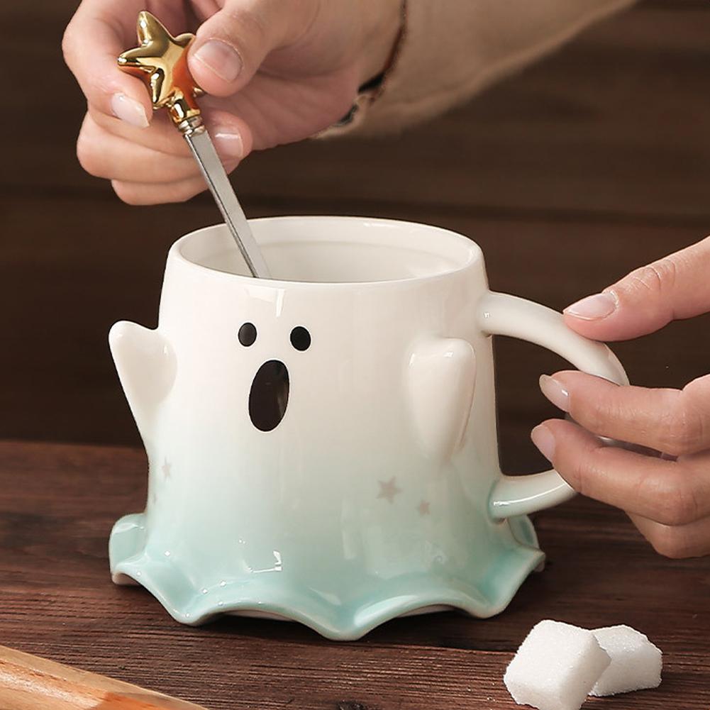 Ghost-shaped ceramic mug with face decal and aqua base; held with gold spoon