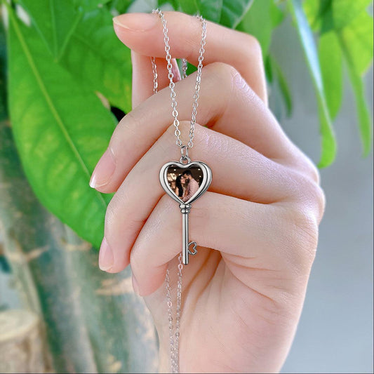 Silver-tone heart locket and key pendant photo necklace on a chain, held in hand