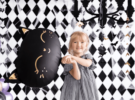 Black cat balloon with gold whiskers held by smiling child in checkered dress