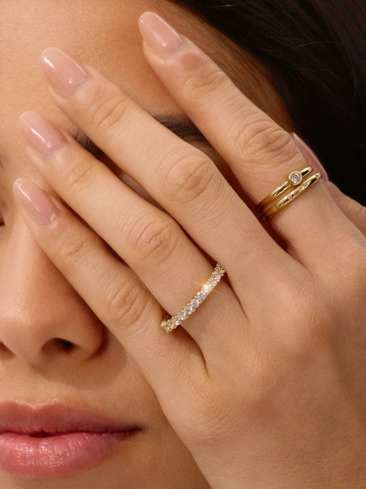 Gold eternity band with clear stones on finger, stacked with slim rings