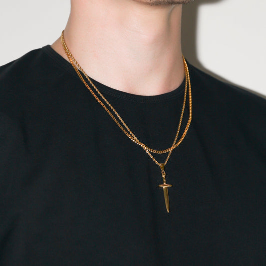 Gold dagger pendant and layered Cuban chain necklaces on neckline, side view