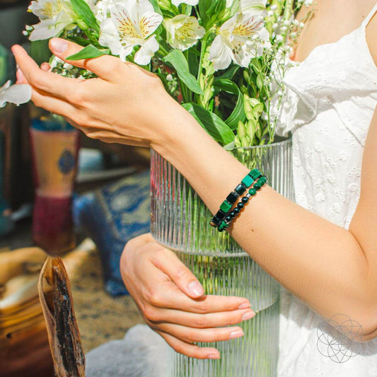 Two beaded bracelets in green and black on a person’s wrist