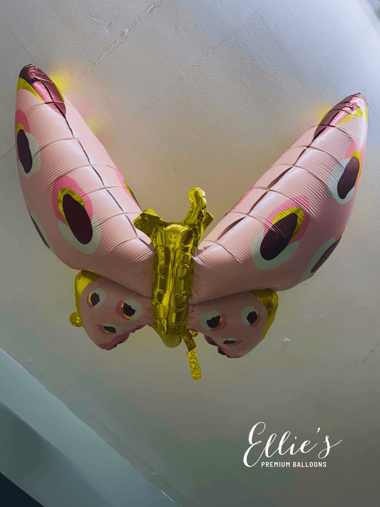 Pink butterfly foil balloon close-up with gold center and dark oval spots.