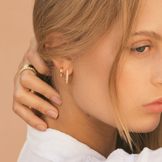 Gold huggie hoop earring with smooth rounded band, close-up on ear