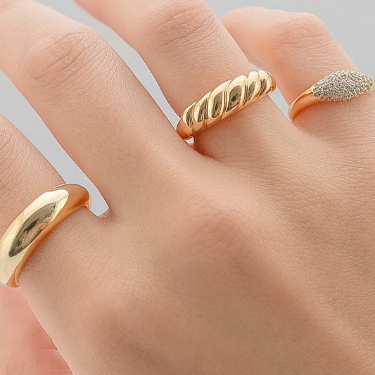 Gold-tone twisted dome band ring on finger, glossy finish with ridged texture