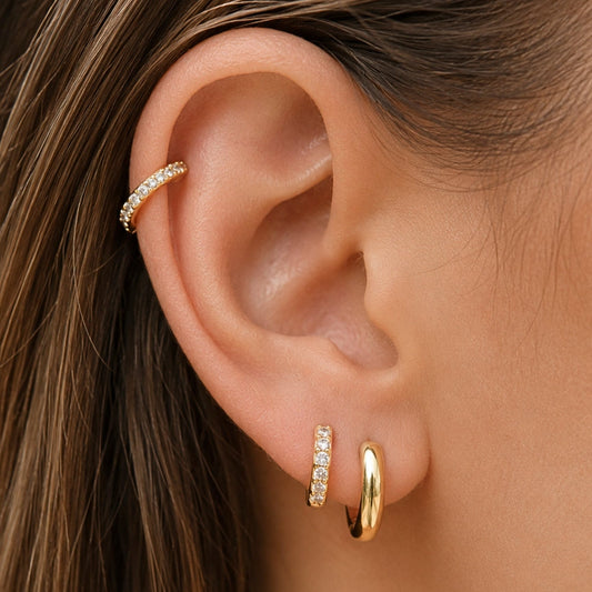 Gold oval huggie hoop earrings shown on ear, small clear-stone accents
