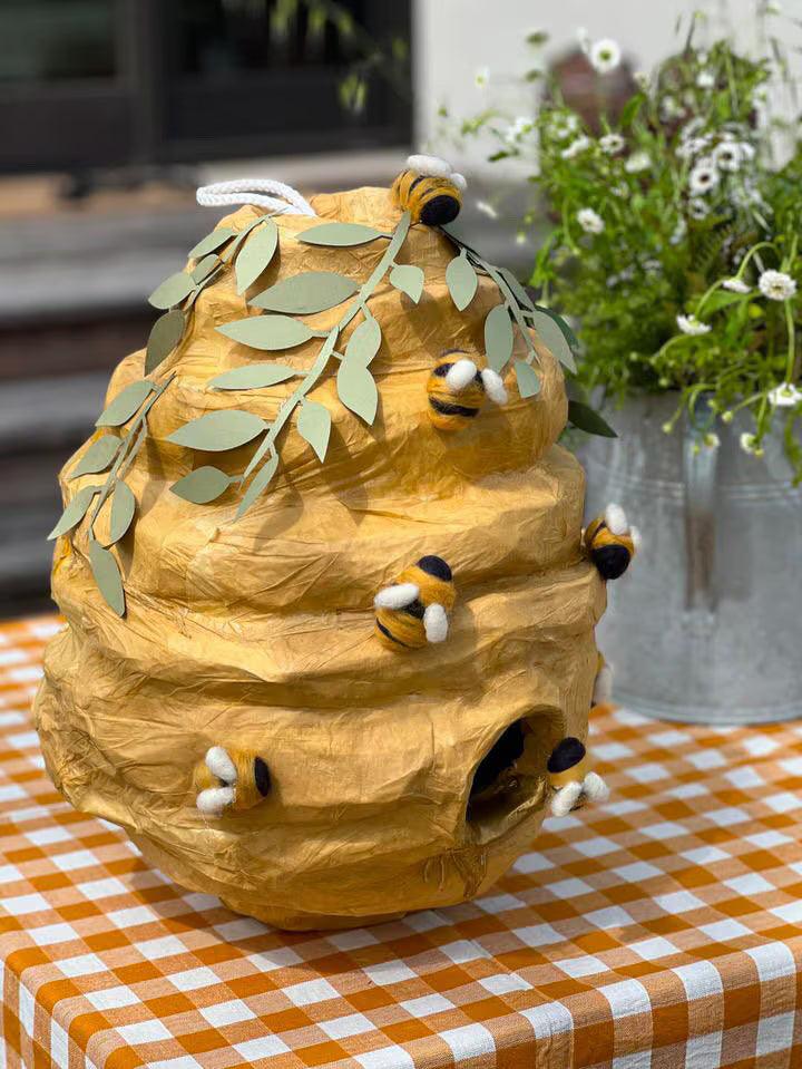 Angled close-up of bee hive piñata with leaf top and plush bees around the holes