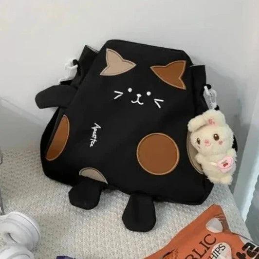 Black cat-shaped messenger bag with cat face, brown circle patch, and plush keychain accessory