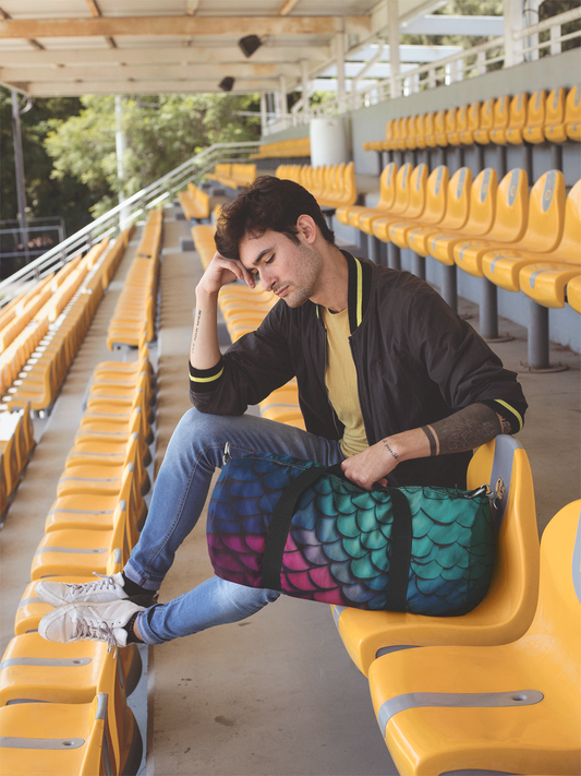 Teal mermaid-scales duffel bag with black strap, set on seats.