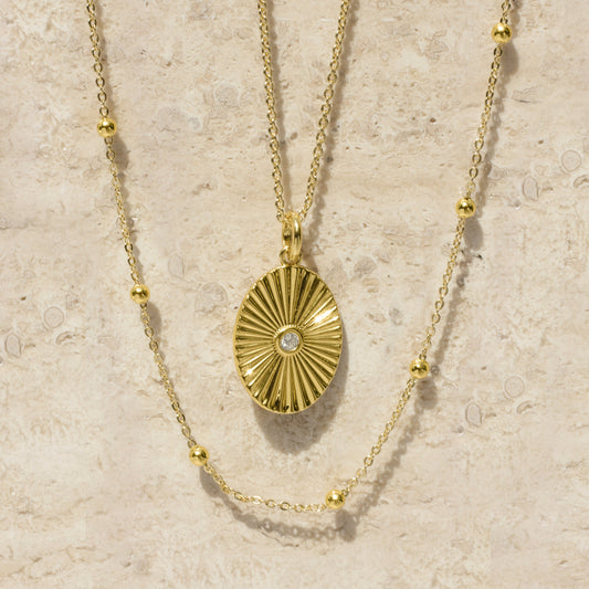 Gold sunburst oval pendant necklace with small round satellite bead accents