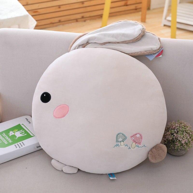 Light grey round plush rabbit pillow with stitched face and folded ears on sofa.