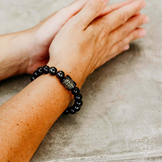 Black bead bracelet with gold square charm, worn on wrist