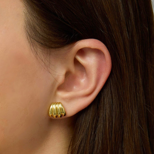 Gold scallop stud earrings on ear with ridged, rounded scallop shape