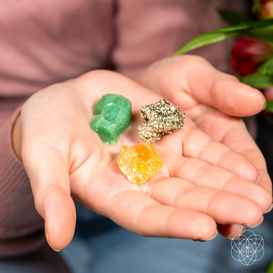 Three assorted crystal stones in hand: green, orange, and gold glitter mineral