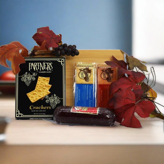 Gourmet board gift set featuring crackers, sausage, and grapes beside autumn leaves on a tray