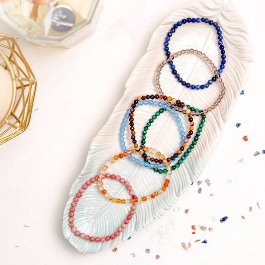 Four multicolor beaded chakra bracelets laid on oval tray: blue, green, pink, orange.