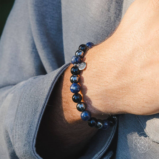 Beaded bracelet on wrist with black and blue beads and a round metal charm pendant