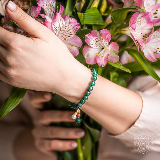 Gemstone bracelet worn on wrist with green beads and a small dangling charm