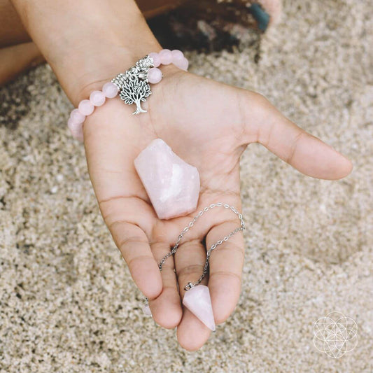 Rose quartz bead bracelet with tree-of-life charm and pink stones, shown on an open hand.