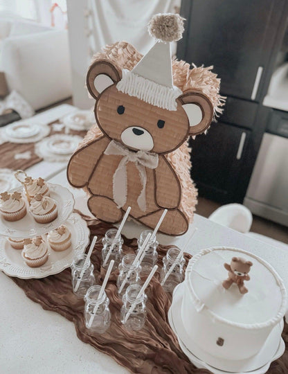 Brauner Teddy mit Geburtstagsmütze und weißem Schleifenhemd am Tisch