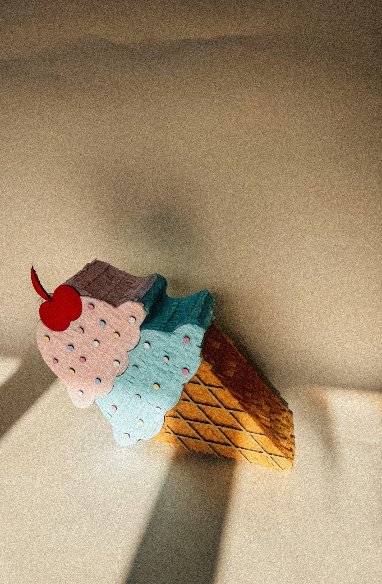 Blue ice cream cone piñata with white sprinkles and red cherry, brown waffle cone