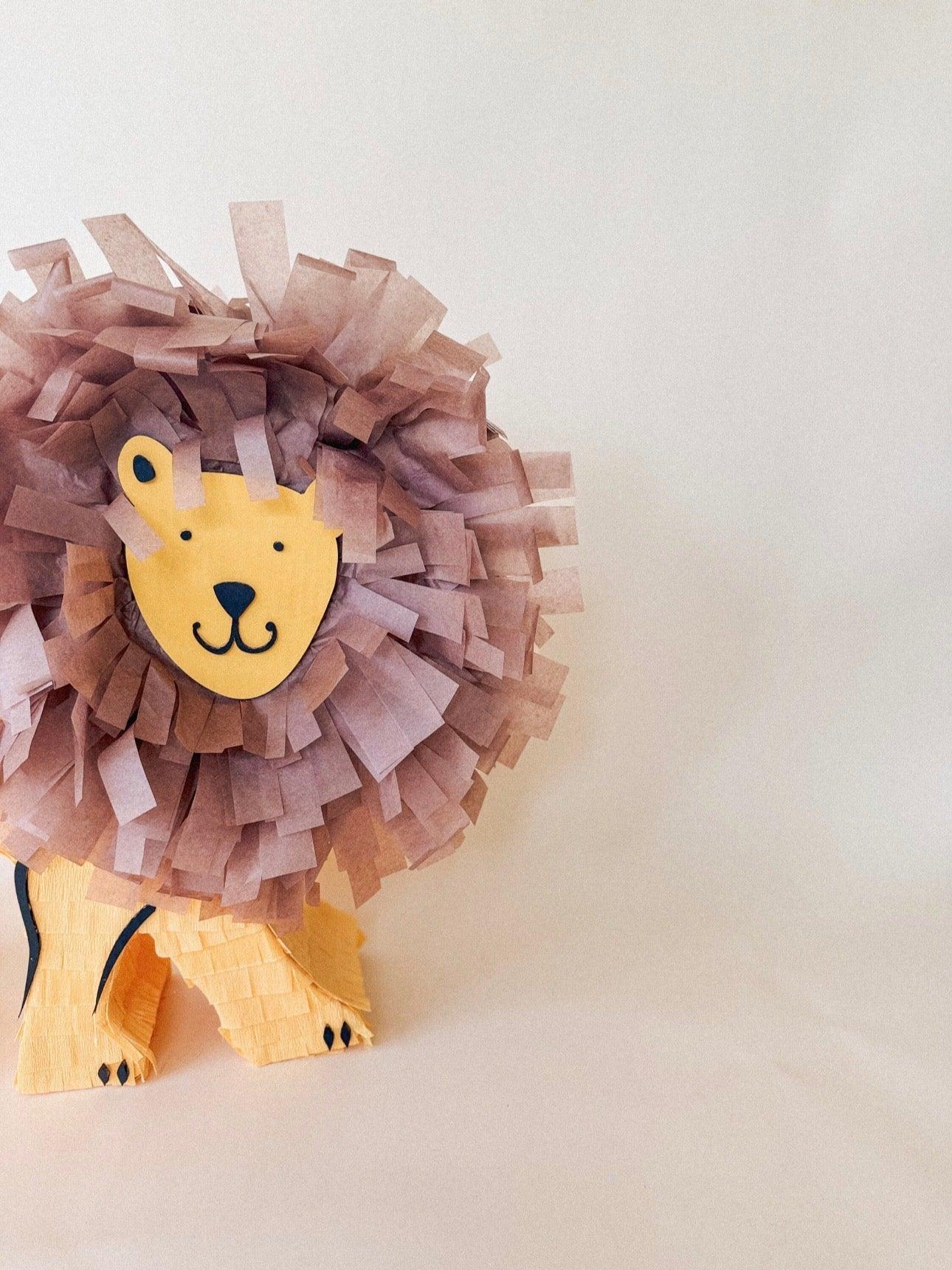 León piñata de pie, melena morada y cara amarilla con ojos y hocico marcados