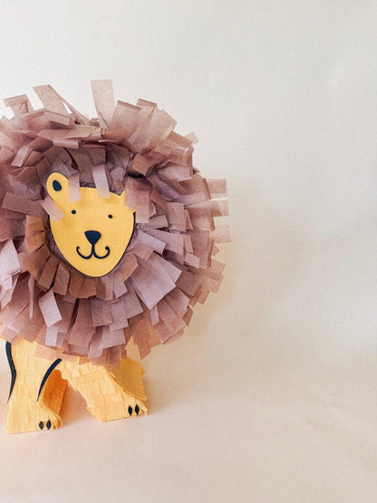 León piñata de pie, melena morada y cara amarilla con ojos y hocico marcados