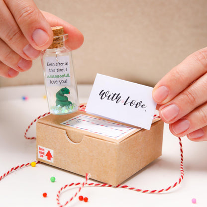 Corked message bottle and 'With love' card held above kraft gift box