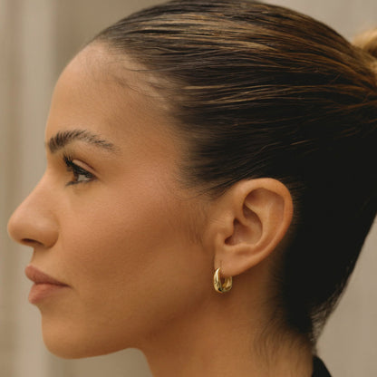 Gold-tone wavy hoop earring on side profile, small hinged hoop