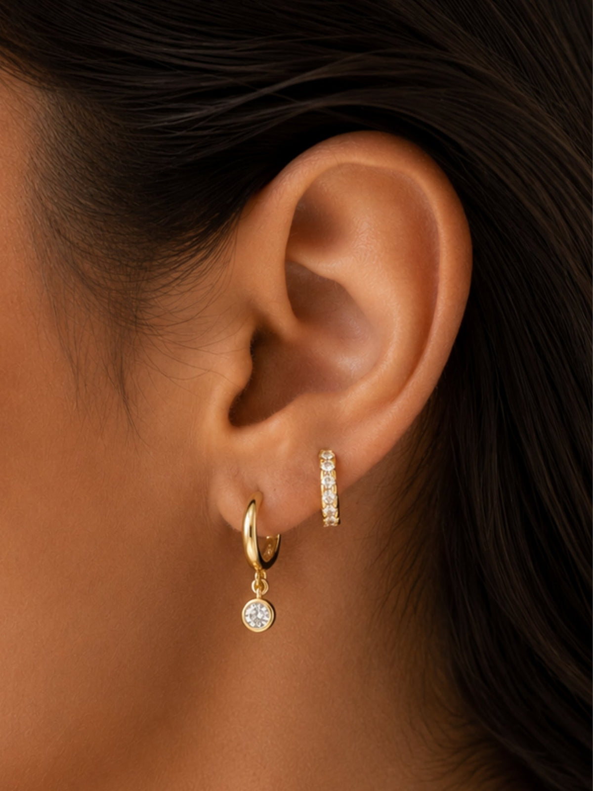 Gold diamond huggie hoops, one with a dangling round stone and one slim pavé hoop
