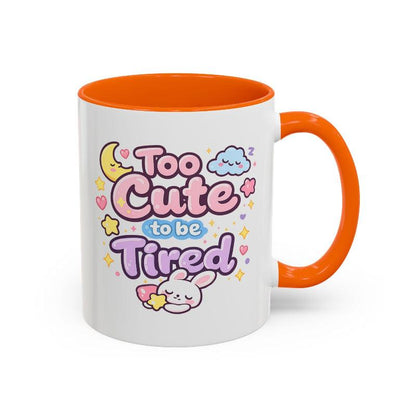 White mug with orange rim and handle, “Too Cute to be Tired” text and bunny.