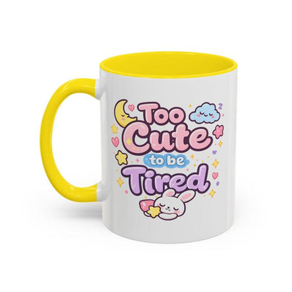 White mug with yellow rim and handle, “Too Cute to be Tired” bunny graphic.
